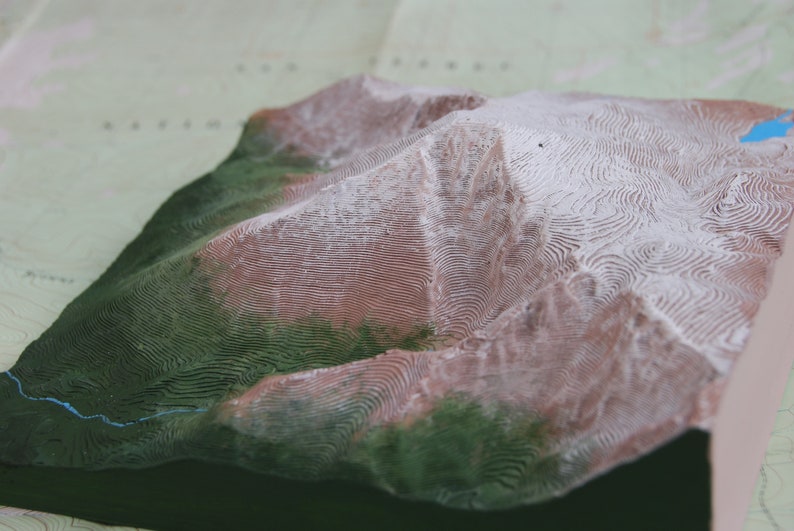 K&ouml;nnte beinhalten: Ein 3D-gedrucktes Modell einer Bergkette mit gr&uuml;nen und wei&szlig;en Details. Das Modell besteht aus einem strukturierten Material und hat ein realistisches Aussehen.