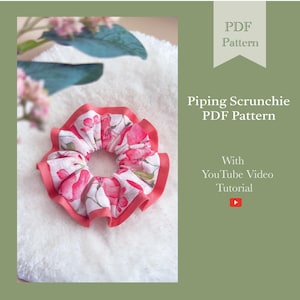 Puede incluir: Una scrunchie floral con ribete rojo y fondo blanco. La scrunchie presenta un estampado de flores rosas. La imagen también incluye el texto "Piping Scrunchie PDF Pattern" y "With YouTube Video Tutorial".