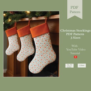 Peut inclure: Trois bas de Noël avec un motif floral et des revers orange sont suspendus à une cheminée en bois. Les bas sont blancs avec un motif répété de fleurs orange et vertes. Le texte indique "Christmas Stockings PDF Pattern 3 Sizes".