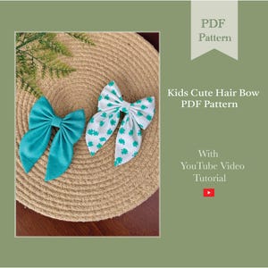 May include: Two fabric hair bows. One is solid teal, the other is white with a teal clover pattern. The bows are on a woven surface with the text "Kids Cute Hair Bow PDF Pattern" and "With YouTube Video Tutorial".