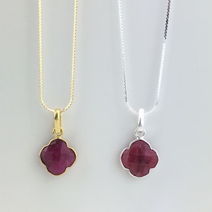 Peut inclure: Deux colliers avec des pendentifs en forme de trèfle. L'un est doré, l'autre argenté. Les deux pendentifs présentent une pierre précieuse rouge foncé facettée. Les chaînes délicates sont suspendues sur un fond neutre.