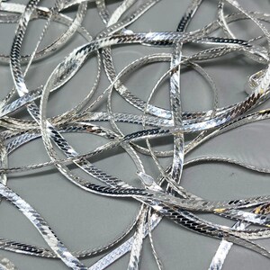 Op de afbeelding: Een zilveren slangenketting met een glanzende, gestructureerde afwerking. De ketting is gemaakt van in elkaar grijpende schakels die een gladde, vloeiende uitstraling cre&euml;ren.