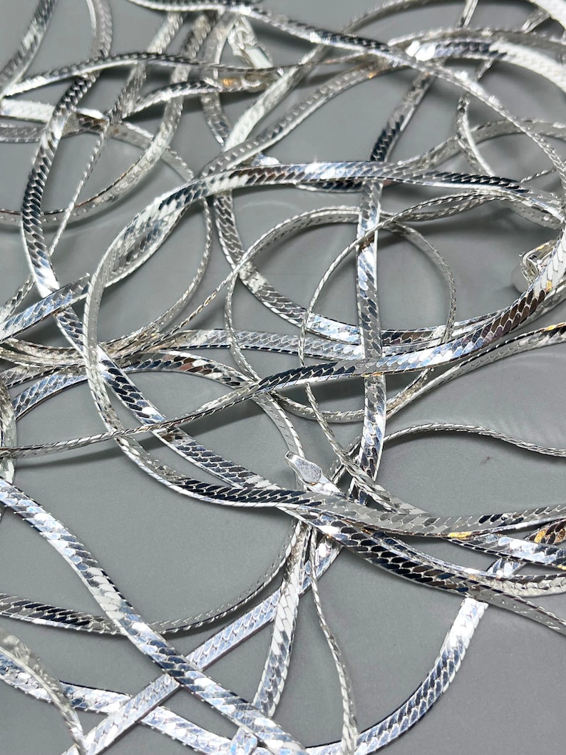 Op de afbeelding: Een zilveren slangenketting met een glanzende, gestructureerde afwerking. De ketting is gemaakt van in elkaar grijpende schakels die een gladde, vloeiende uitstraling cre&euml;ren.