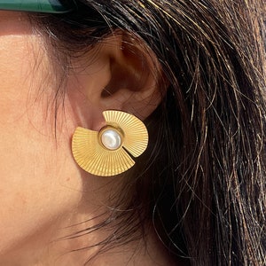 May include: Gold tone earrings with a fan-shaped design and a white pearl accent.