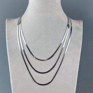 Op de afbeelding: Een zilveren ketting met vier strengen van verschillende lengtes. De ketting wordt getoond op een witte mannequinbuste.