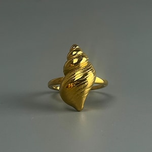 May include: A gold-coloured ring featuring a seashell design. The ring is made of metal and has a smooth, polished finish.