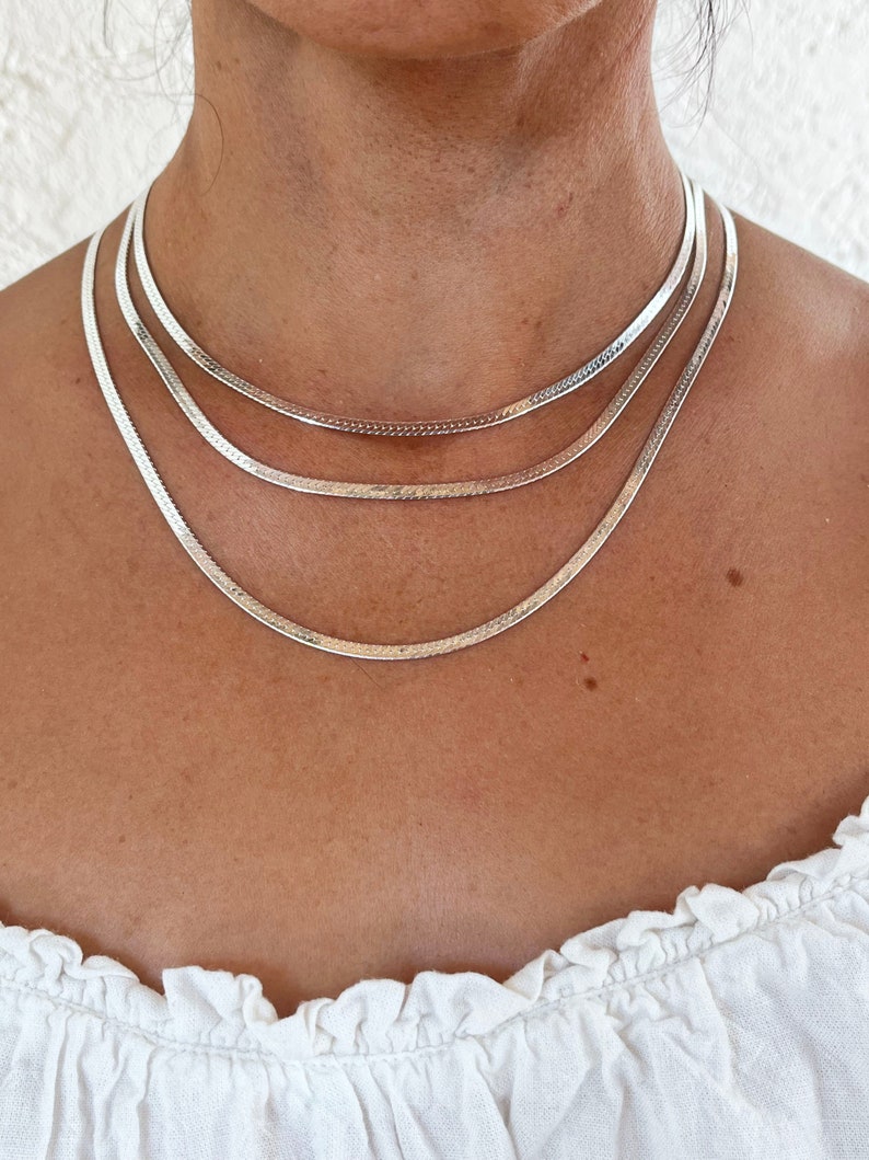 Op de afbeelding: Een zilveren ketting met drie verschillende breedtes ketting. De ketting is gelaagd op de nek van een persoon.