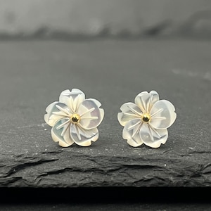 Peut inclure: Une paire de boucles d'oreilles en nacre blanche en forme de fleur avec des accents dorés. Les boucles d'oreilles sont petites et délicates, et elles feraient un beau cadeau.