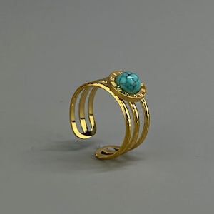Op de afbeelding: Gouden ring met drie banden en een turquoise steen in een ronde zetting.