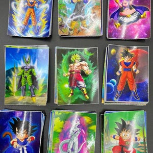 May include: Nine colourful trading cards featuring characters from the Dragon Ball anime series. The cards showcase various characters in action poses, with vibrant backgrounds and dynamic energy effects. The cards are stacked on a dark surface.