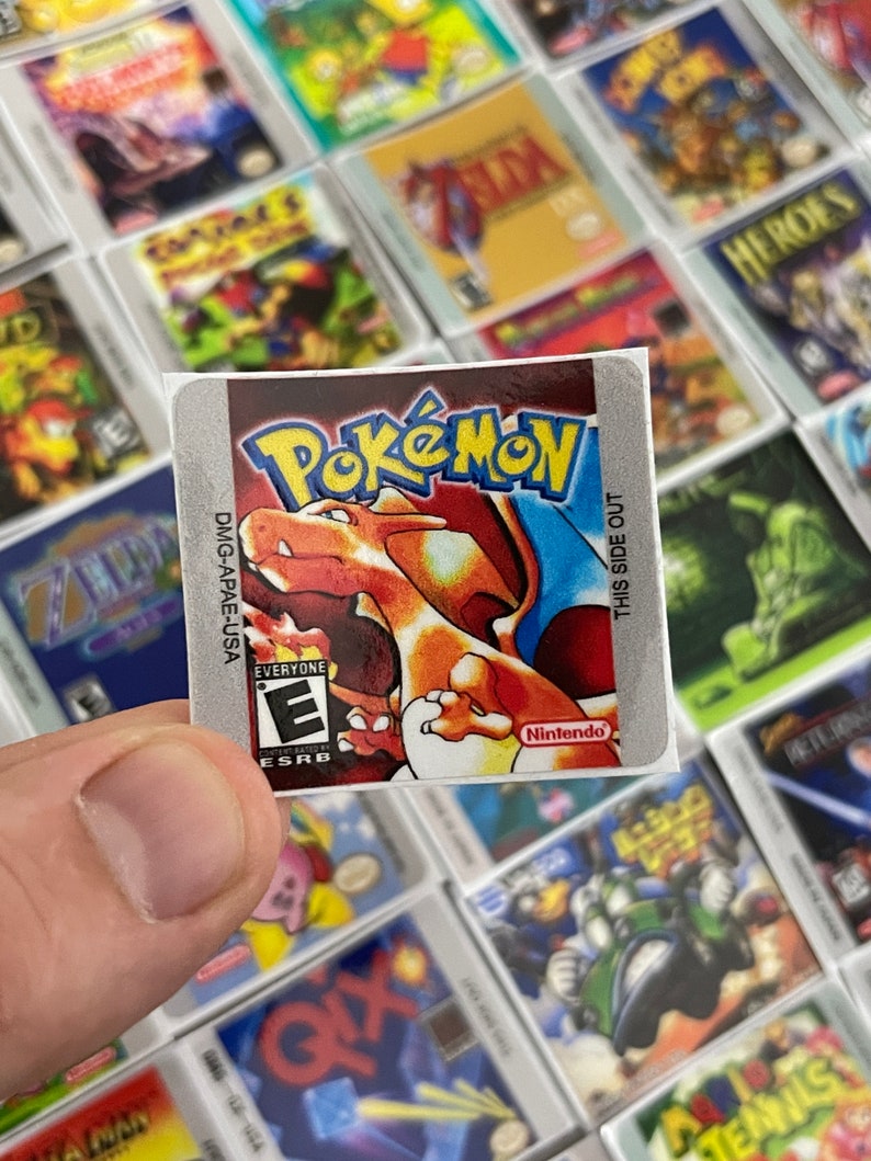 K&ouml;nnte beinhalten: Eine Nahaufnahme eines Pokemon-Videospiel-Kartuschen-Etiketts. Das Etikett ist silberfarben mit einem roten, orangefarbenen und gelben Bild eines Pokemon-Charakters. Das Etikett enth&auml;lt auch den Text "Pokemon", "Nintendo", "Jedermann" und "ESRB".
