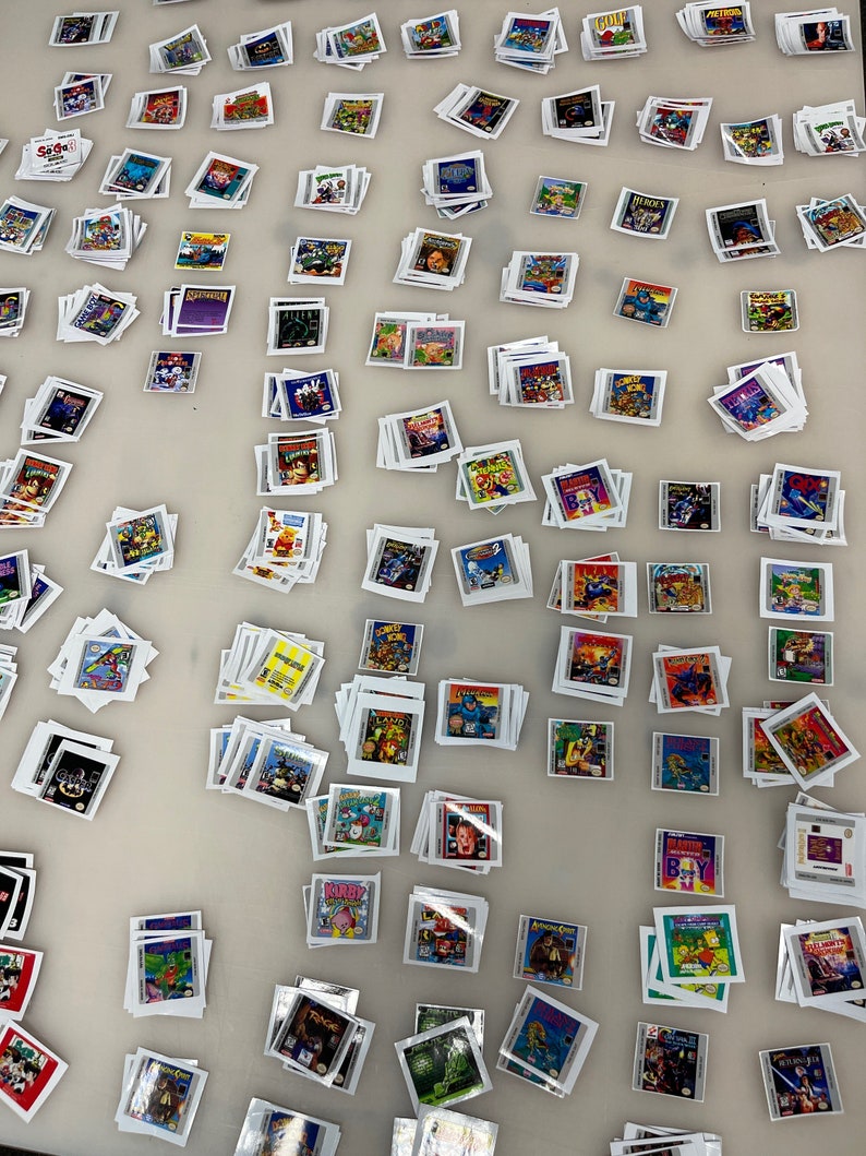 K&ouml;nnte beinhalten: Eine gro&szlig;e Sammlung von Vintage-Videospielkassetten, die auf einer wei&szlig;en Oberfl&auml;che gestapelt und angeordnet sind. Die Kassetten stammen vom Super Nintendo Entertainment System (SNES) und zeigen verschiedene beliebte Titel, darunter "Kirby", "Super Mario World", "Street Fighter II" und "Donkey Kong Country".