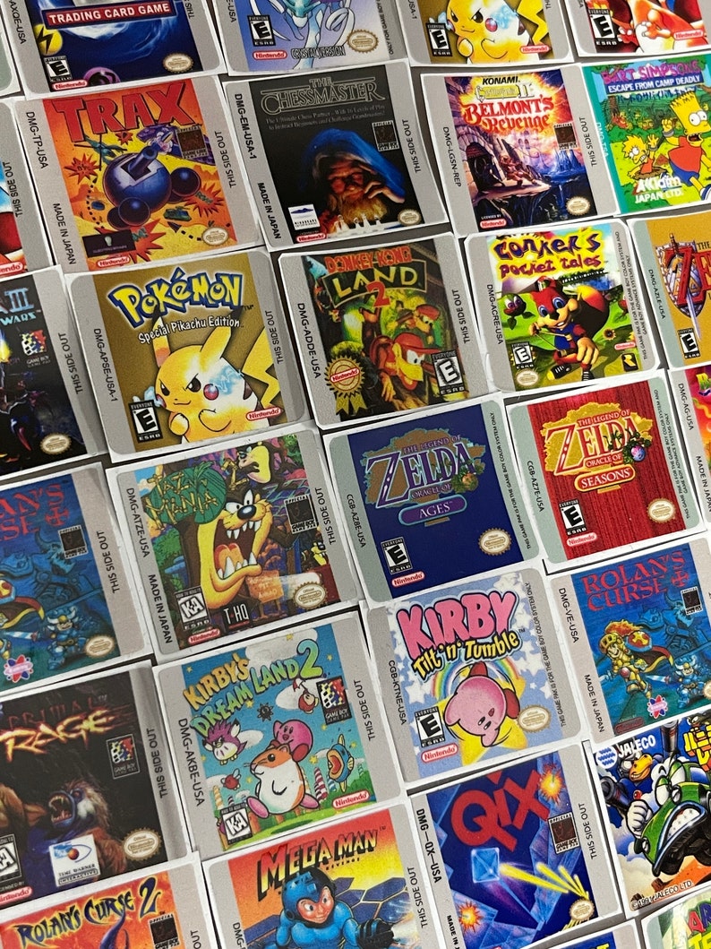 K&ouml;nnte beinhalten: Eine Sammlung bunter Game Boy-Spielekartuschen-Etiketten. Die Etiketten zeigen verschiedene Spieltitel, darunter "Pok&eacute;mon Special Pikachu Edition", "The Legend of Zelda: Oracle of Ages", "Kirby Tilt 'n' Tumble" und "Mega Man".