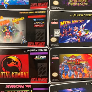 K&ouml;nnte beinhalten: Eine Sammlung von Super Nintendo-Spielkassetten. Zu den Titeln geh&ouml;ren "Mega Man X2", "Mortal Kombat", "Ultimate Mortal Kombat" und "Mega Action Heroes". Die Kassetten zeigen farbenfrohe Spielgrafiken und Logos.
