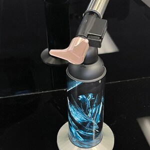 May include: A black and silver torch with a blue and white floral design on the canister. The torch is on a gray stand.