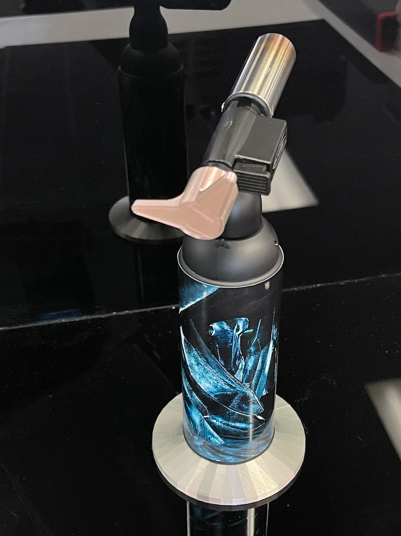 May include: A black and silver torch with a blue and white floral design on the canister. The torch is on a gray stand.