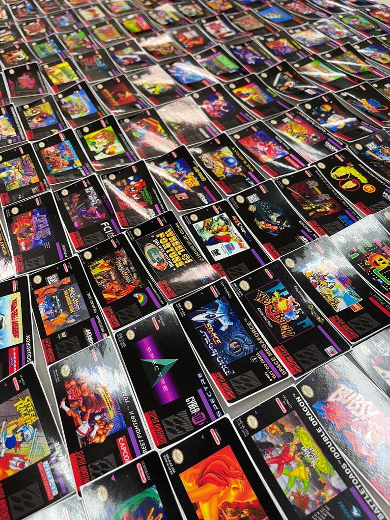 K&ouml;nnte beinhalten: Eine Sammlung von Super Nintendo-Spielkassetten mit verschiedenen Spieletiteln und farbenfrohen Cover-Artworks. Die Kassetten sind eng angeordnet und zeigen eine Vielzahl von Spielgenres und -designs. Das Bild wurde aus einem hohen Winkel aufgenommen.