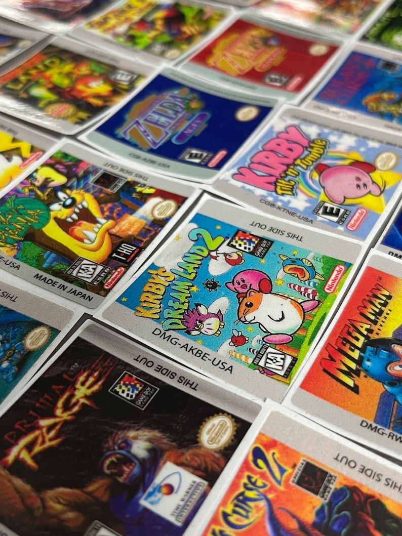 K&ouml;nnte beinhalten: Eine Sammlung von bunten Game Boy-Spielekartuschen-Etiketten. Die Etiketten zeigen verschiedene Charaktere und Titel, darunter Kirby's Dream Land 2, Mega Man und Primal Rage. Die Etiketten sind auf silbernem Hintergrund mit schwarzem Text gedruckt.