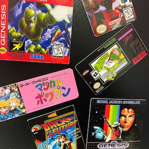 K&ouml;nnte beinhalten: Eine Sammlung von Videospiel-Kartuschenboxen f&uuml;r verschiedene Konsolen, darunter Sega Genesis, Super Nintendo und Nintendo 64. Die Boxen zeigen farbenfrohe Grafiken und Logos, darunter "Vectorman", "Starfox", "Boogerman", "Zur&uuml;ck in die Zukunft" und "Michael Jackson's Moonwalker".