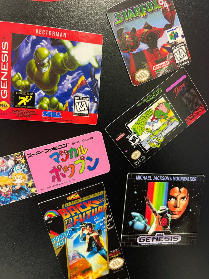 K&ouml;nnte beinhalten: Eine Sammlung von Videospiel-Kartuschenboxen f&uuml;r verschiedene Konsolen, darunter Sega Genesis, Super Nintendo und Nintendo 64. Die Boxen zeigen farbenfrohe Grafiken und Logos, darunter "Vectorman", "Starfox", "Boogerman", "Zur&uuml;ck in die Zukunft" und "Michael Jackson's Moonwalker".