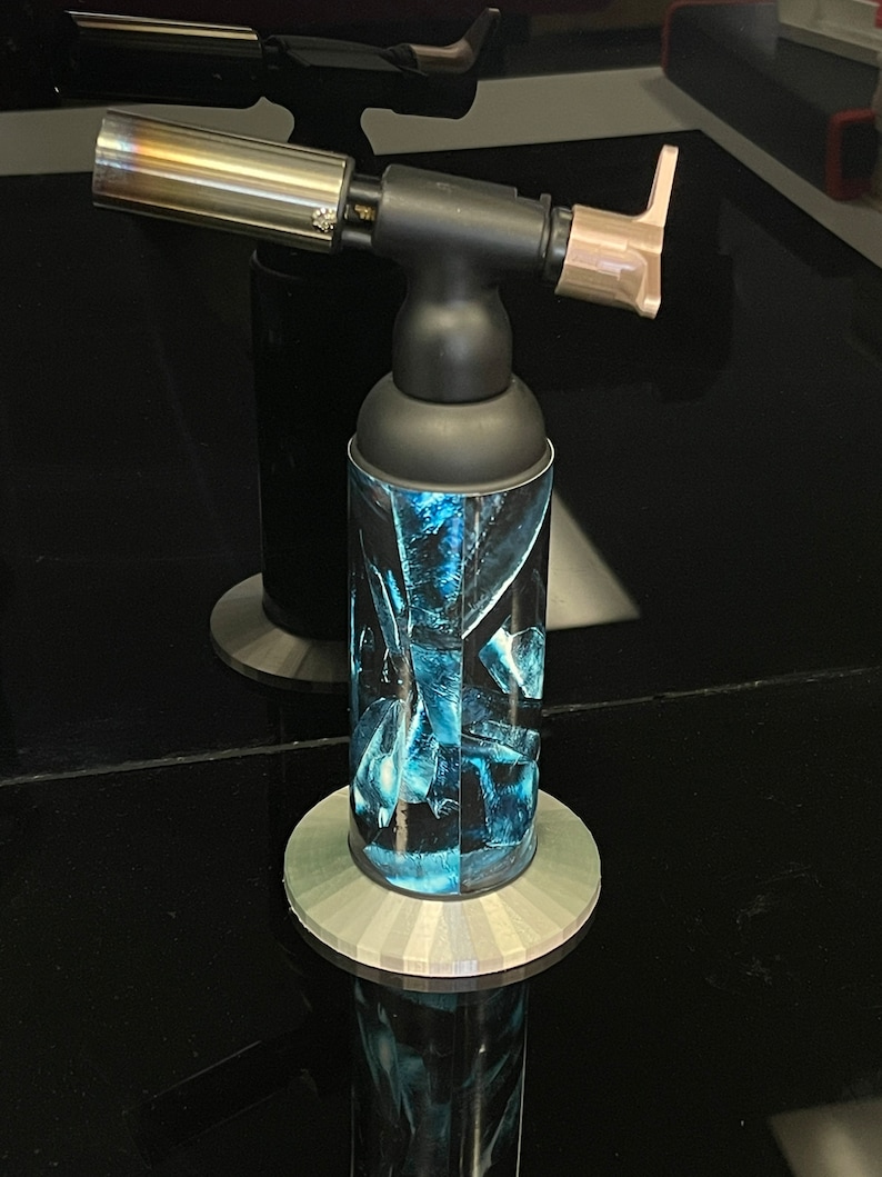 May include: A black and silver torch with a blue and black patterned design. The torch has a long, silver nozzle and a black handle.