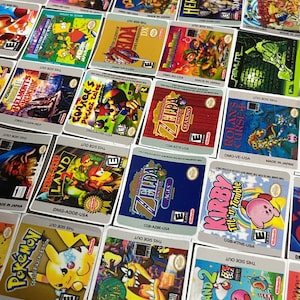 K&ouml;nnte beinhalten: Eine Sammlung von bunten Game Boy-Spielekartuschen-Etiketten mit beliebten Titeln wie Zelda, Donkey Kong, Pokemon, Kirby und mehr. Die Etiketten sind auf wei&szlig;em Papier mit schwarzem Text und Grafiken gedruckt.