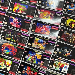 K&ouml;nnte beinhalten: Eine Sammlung von Super Nintendo-Spielkassetten mit verschiedenen Titeln und farbenfrohen Cover-Art. Zu den Spielen geh&ouml;ren "Super Metroid", "Aladdin", "Sonic Blastman II" und "Wheel of Fortune Deluxe Edition". Die Kassetten sind schwarz mit lila und wei&szlig;em Text.