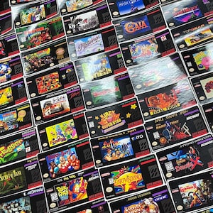 K&ouml;nnte beinhalten: Eine Sammlung von Super Nintendo Entertainment System (SNES) Spielkassetten. Die Kassetten zeigen farbenfrohe Spielbox-Art mit Titeln wie "Mortal Kombat" und "Earthbound". Die Spiele sind auf einer reflektierenden Oberfl&auml;che angeordnet.