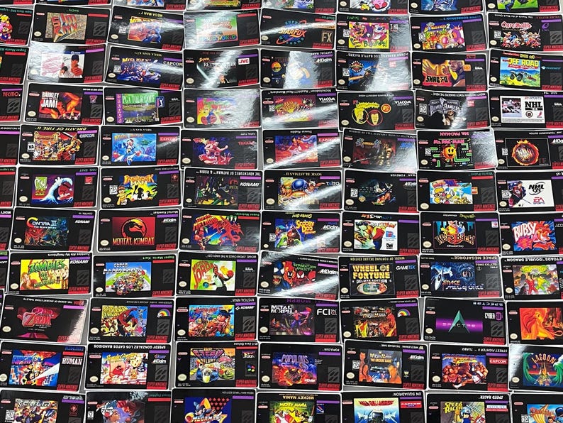 K&ouml;nnte beinhalten: Eine Sammlung von Retro-Super-Nintendo-Spielkassetten. Die Kassetten zeigen farbenfrohe Spielgrafiken und -titel, darunter "Mortal Kombat", "Street Fighter" und "NHL Hockey". Die Kassetten sind eng aneinandergereiht und bilden ein gitterartiges Muster.
