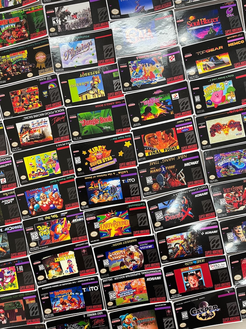 K&ouml;nnte beinhalten: Eine Sammlung von Super Nintendo-Spielkassetten, jede mit einzigartigem Cover-Art. Titel sind u.a. "Donkey Kong Country", "Pilotwings", "Paperboy", "Jungle Book", "Kirby Super Star", "Final Fight", "Earthbound" und "Harvest Moon". Die Kassetten sind schwarz mit farbenfrohen Spielgrafiken.