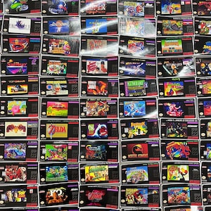 K&ouml;nnte beinhalten: Eine Sammlung von Spielmodulen f&uuml;r das Super Nintendo Entertainment System (SNES). Die Module zeigen farbenfrohe Spielbox-Artworks und Titel wie "Zelda", "Mortal Kombat" und "Mario World". Die Spiele werden vor einem schwarzen Hintergrund pr&auml;sentiert.