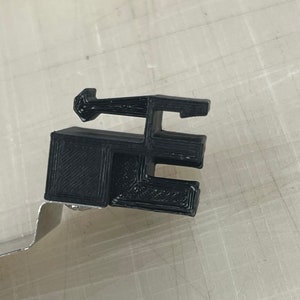 Peut inclure: Pièce en plastique noire imprimée en 3D avec une base rectangulaire et un dessus incurvé.