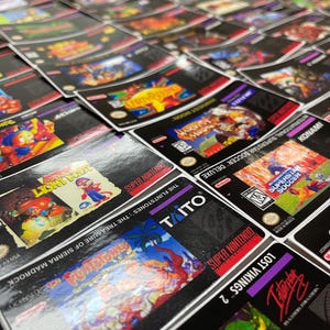 K&ouml;nnte beinhalten: Nahaufnahme einer Sammlung von Super Nintendo-Spielmodulen. Die Boxen zeigen farbenfrohe Kunstwerke von Spielen wie "The Flintstones: The Treasure of Sierra Madrock" und "Harvest Moon". Die Module sind eng aneinandergereiht.