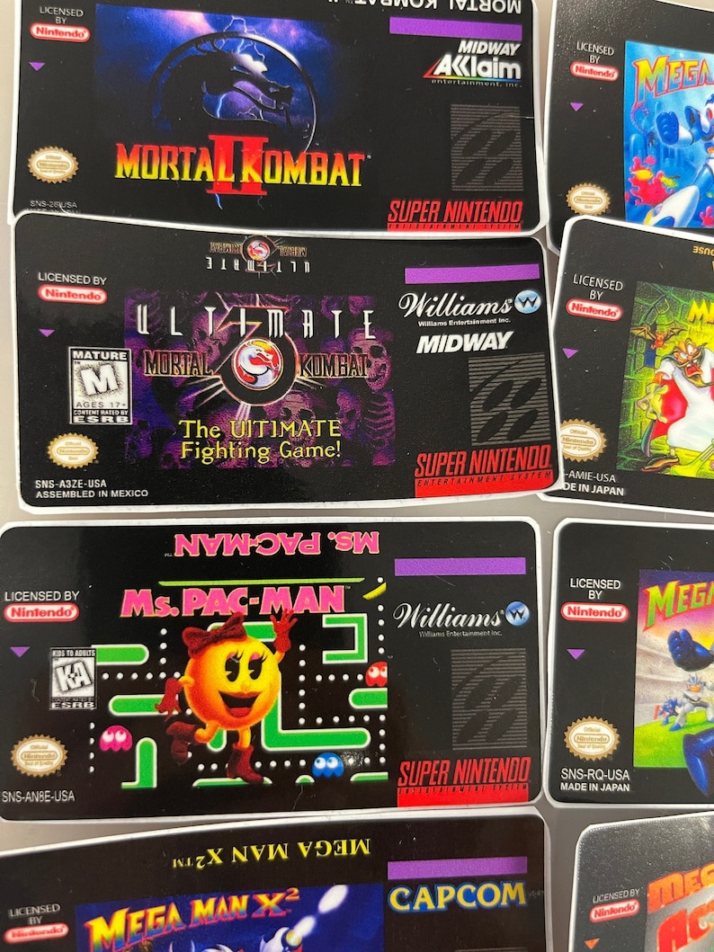 K&ouml;nnte beinhalten: Eine Sammlung von Super Nintendo-Spielkassetten, darunter "Mortal Kombat II", "Ultimate Mortal Kombat" und "Ms. Pac-Man". Die Kassetten zeigen farbenfrohe Spielgrafiken und Logos auf schwarzem Hintergrund. Die Spiele sind von Nintendo lizenziert.