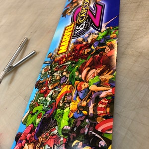 May include: A colorful arcade cabinet marquee featuring a large number "2" and the text "MARVEL VS. CAPCOM 2" with a background of many characters from the Marvel and Capcom universes.