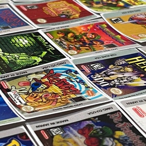 K&ouml;nnte beinhalten: Eine Sammlung von bunten Nintendo Game Boy Advance-Spielkassetten. Die Kassetten sind in einem Raster angeordnet und zeigen verschiedene Spieltitel, darunter "Pok&eacute;mon", "Kirby's Dream Land" und "The Legend of Zelda".