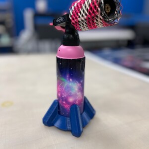 May include: A pink and black torch with a galaxy print design and a blue base. The torch has a white and red mesh covering the nozzle.