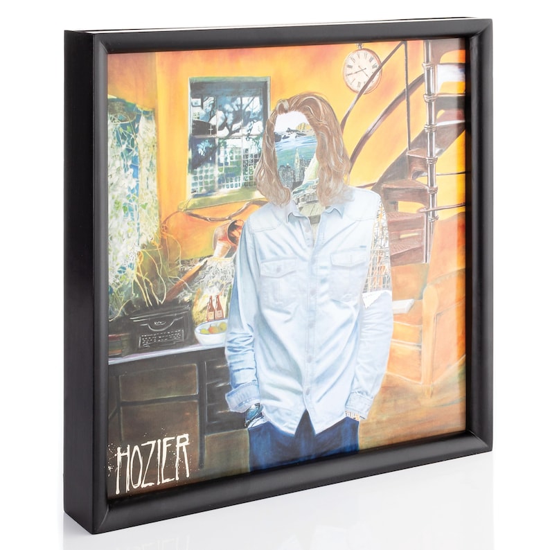 Op de afbeelding: Een ingelijste albumhoes met een man met lang haar die in een kamer staat met een gele muur, een raam en een trap. De albumhoes is getiteld "Hozier".