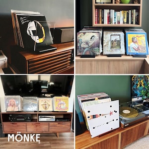 May include: A collection of vinyl record albums displayed on wooden furniture. The albums are in clear acrylic stands. The image includes a Daft Punk album cover, and the word "M&Ouml;NKE" is visible in the bottom left corner.