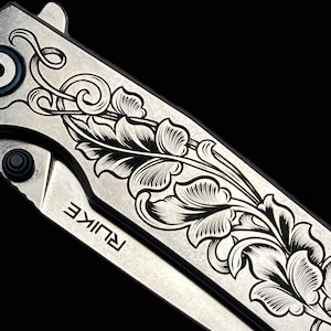 May include: A silver pocket knife with a floral design etched into the blade. The knife has a black handle and the word "RUINKE" is engraved on the blade.
