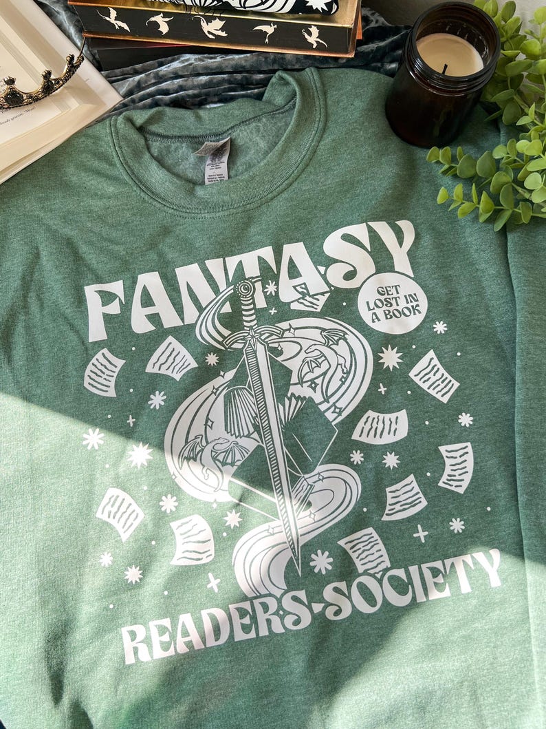May include: A green sweatshirt with a white graphic design of a sword, book, and swirling smoke. The text "Fantasy Readers Society" and "Get Lost in a Book" are also included in the design.