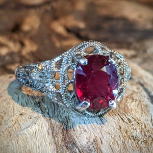May include: A silver ring with a large, oval-shaped ruby gemstone set in a filigree design.