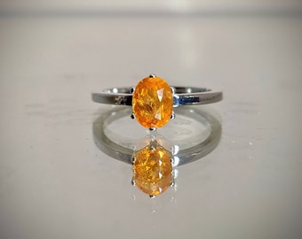 May include: A silver ring with an oval-shaped orange gemstone set in a prong setting.