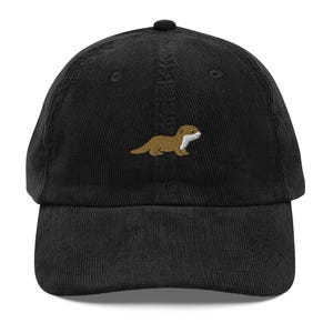 May include: A black corduroy baseball cap featuring an embroidered graphic of a brown otter with a white chest and face. The cap has a structured crown, a curved brim, and a button at the top centre. The embroidery is centred on the front panel.