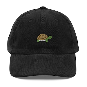 May include: A black corduroy baseball cap featuring a small, centered embroidery of a green and brown turtle. The cap has a structured crown, a curved brim, and a button at the top, showcasing a textured fabric finish throughout the design.