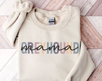 May include: A beige sweatshirt with the text "Greyhound mama" in colorful letters. The letters are in shades of pink, yellow, blue, and gray.
