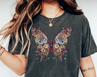Peut inclure: Un t-shirt gris foncé avec un motif de papillon coloré fait de fleurs. Le papillon est centré sur le t-shirt. Le mannequin porte un jean bleu et des baskets blanches.