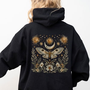 Puede incluir: Sudadera con capucha negra con un estampado gráfico de una polilla, luna y estrellas en la espalda. El gráfico es en oro y blanco.