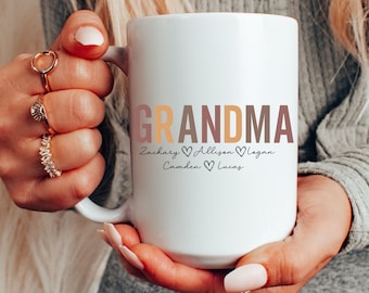 May include: White ceramic coffee mug with the word "Grandma" in pink, orange, and brown lettering. Below the word "Grandma" are the names "Zachary, Allison, Logan, Camden, Lucas" with hearts between each name.
