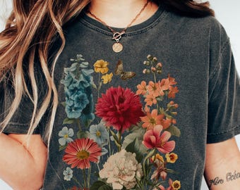 May include: Dark gray t-shirt featuring a vibrant floral design with red, pink, blue, and yellow flowers, and a butterfly. The shirt has a vintage, washed look. The word "Pepper" is in a yellow circle.